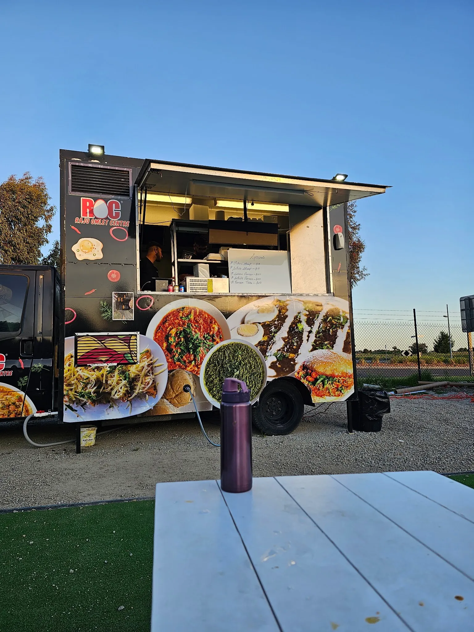 The ROC food truck at dusk, its serving hatch lit up with a specials board and a vendor at work inside.