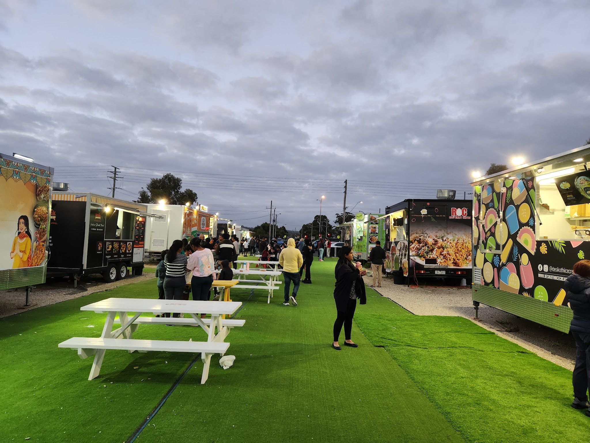 Officer Food Truck Park at dusk with lit-up trucks, string lights and picnic tables full of visitors