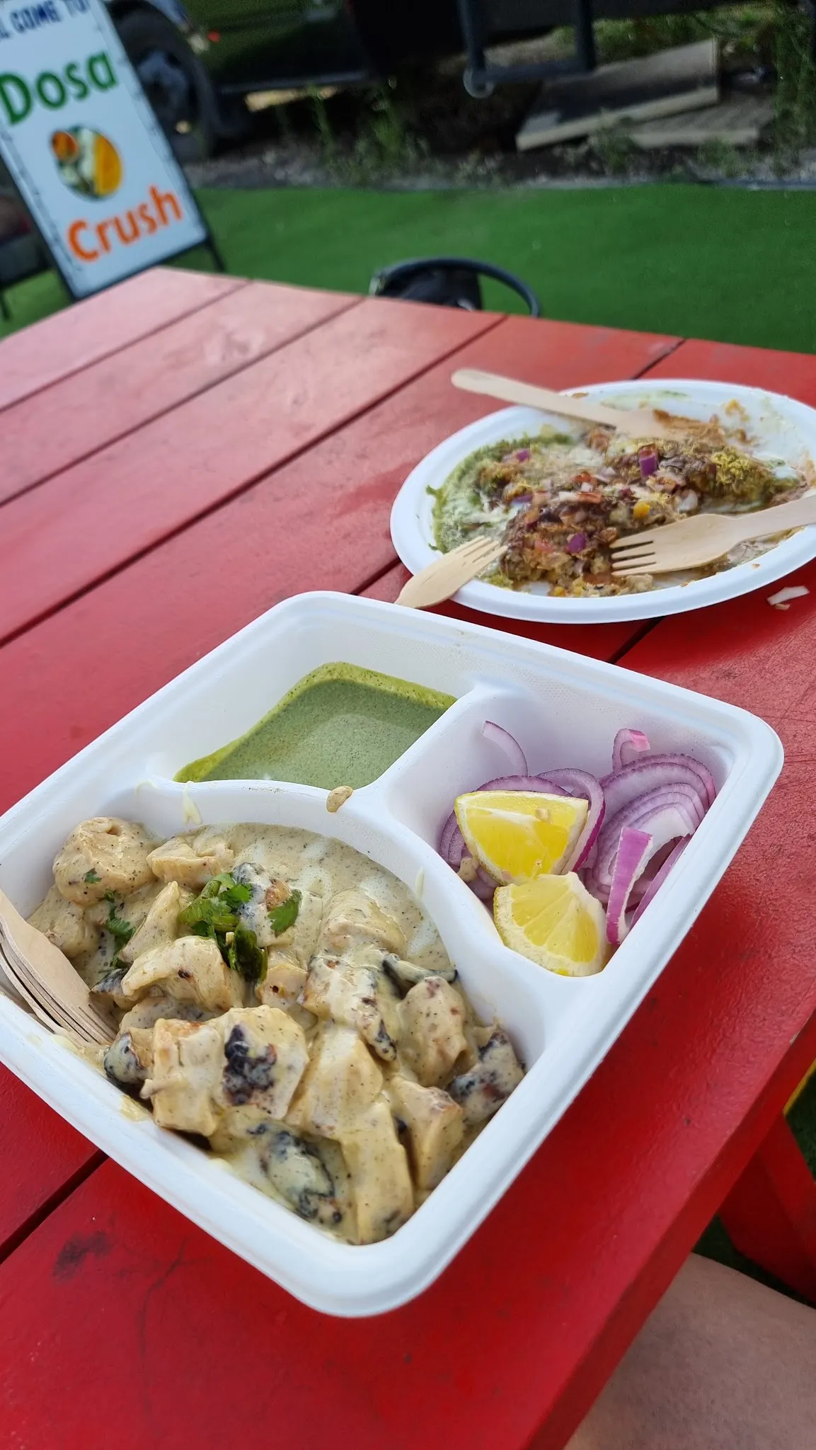 A tray of creamy chicken tikka with pita, pickled onion and lemon at a picnic table.